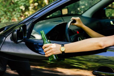 Araba kullanırken elinde bir şişe alkol tutan bir kadın sürücü.