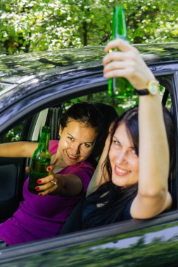 Arabada bira şişeleri tutan ve kameraya bakan mutlu bir kadın. 