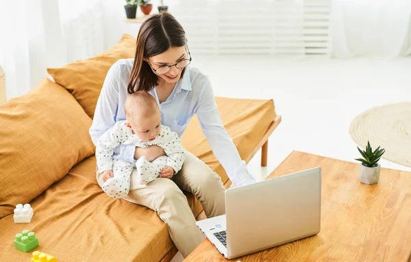 幼児の新生児の赤ちゃんの息子を持つ若いシングルマザーラップトップを使用して ウェブを検索し 一緒に漫画を見ています 産前産後の休暇やフリーランスで子供用品を探す — ストック写真