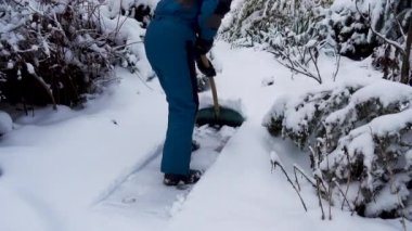 Mutlu genç kadın evin yakınındaki bahçede kar temizliyor. Elinde kar küreği olan bir kızın portresi. Mutlu kız bahçedeki evin yakınındaki karı kaldırıyor. Mutluluk kavramı, neşe. 