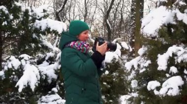 Kışın elinde kamera olan genç bir kadının portresi. Kız kışın fotoğraflarını çekiyor. Karlı bir parkta kamerası olan mutlu genç bir kadın.. 