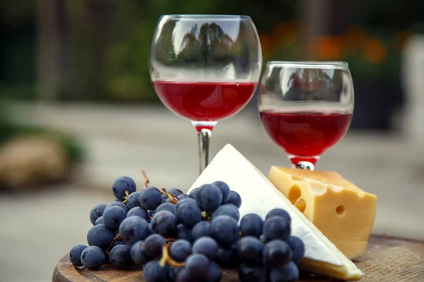 Composition with a glass of red wine, grapes and cheese. Red natural wine, cheese and a bunch of grapes in a garden in nature.