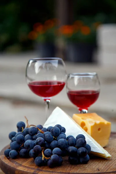 Composition with a glass of red wine, grapes and cheese. Red natural wine, cheese and a bunch of grapes in a garden in nature.