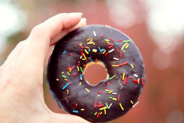 Bir kadının eli taze pişmiş, parlak renkli jöleli bir çöreği tutuyor. Renkli bir donut şeklinde tatlı bir tatlıyı tutan el.. 