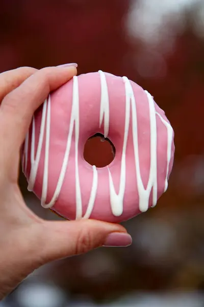 Bir kadının eli taze pişmiş, parlak renkli jöleli bir çöreği tutuyor. Renkli bir donut şeklinde tatlı bir tatlıyı tutan el.. 