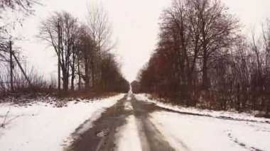 Bir araba penceresinden kışın karlı bir kır yolu manzarası. Kışın karlı bir kır yolunda araba sürmek. Orman, tarla kış yolu. 