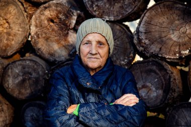 Yaşlı bir kadının portresi eski bir odunun arka planında. Yakacak odunların arka planında şapkalı yaşlı bir kadının yüzü.. 