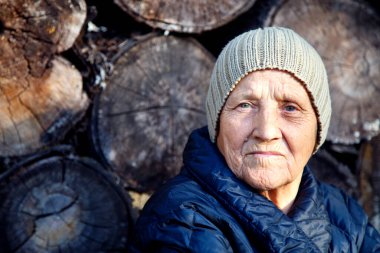 Yaşlı bir kadının portresi eski bir odunun arka planında. Yakacak odunların arka planında şapkalı yaşlı bir kadının yüzü.. 