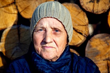 Yaşlı bir kadının portresi eski bir odunun arka planında. Yakacak odunların arka planında şapkalı yaşlı bir kadının yüzü.. 