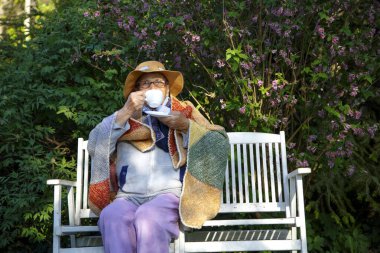 Bahçedeki bankta elinde bir kupa çayla yaşlı bir kadın. Parktaki bankta oturup çay içen mutlu yaşlı kadın. Yaşlılık, bakım, yardım kavramı.