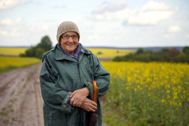Kolza tohumu tarlasında yaşlı bir kadının portresi. Çiçek açan kolza tohumu tarlasında yürüyen mutlu yaşlı kadın. Dinlenme, rahatlama, mutluluk kavramı.. 