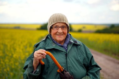 Kolza tohumu tarlasında yaşlı bir kadının portresi. Çiçek açan kolza tohumu tarlasında yürüyen mutlu yaşlı kadın. Dinlenme, rahatlama, mutluluk kavramı.. 
