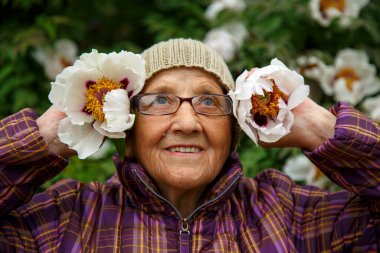 Parktaki bir bankta elinde şakayık çiçeğiyle yaşlı bir kadın. Pansiyonda kalan yaşlı bir kadın hayatın tadını çıkarır. Bakım, yaşlılık ve mutluluk kavramı.. 
