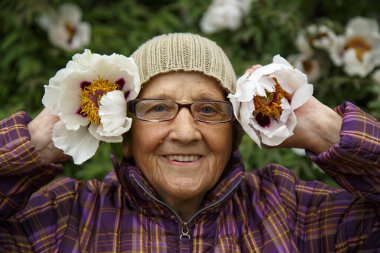 Parktaki bir bankta elinde şakayık çiçeğiyle yaşlı bir kadın. Pansiyonda kalan yaşlı bir kadın hayatın tadını çıkarır. Bakım, yaşlılık ve mutluluk kavramı.. 