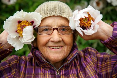 Parktaki bir bankta elinde şakayık çiçeğiyle yaşlı bir kadın. Pansiyonda kalan yaşlı bir kadın hayatın tadını çıkarır. Bakım, yaşlılık ve mutluluk kavramı.. 
