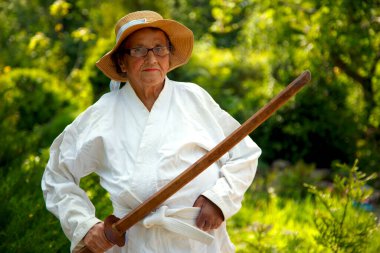 Parkta katanalı bir kimono giymiş yaşlı bir kadın. Bahçede katana ile antrenman yapan yaşlı bir kadının portresi. Yaşlılık, spor, doğa kavramı.. 