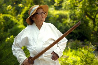 Parkta katanalı bir kimono giymiş yaşlı bir kadın. Bahçede katana ile antrenman yapan yaşlı bir kadının portresi. Yaşlılık, spor, doğa kavramı.. 
