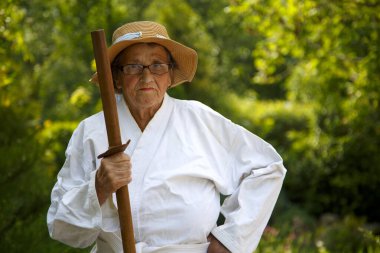 Parkta katanalı bir kimono giymiş yaşlı bir kadın. Bahçede katana ile antrenman yapan yaşlı bir kadının portresi. Yaşlılık, spor, doğa kavramı.. 