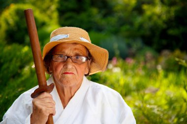 Parkta katanalı bir kimono giymiş yaşlı bir kadın. Bahçede katana ile antrenman yapan yaşlı bir kadının portresi. Yaşlılık, spor, doğa kavramı.. 