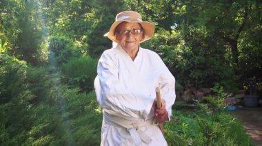 Parkta katanalı bir kimono giymiş yaşlı bir kadın. Bahçede katana ile antrenman yapan yaşlı bir kadının portresi. Yaşlılık, spor, doğa kavramı..  