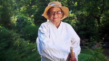 Parkta katanalı bir kimono giymiş yaşlı bir kadın. Bahçede katana ile antrenman yapan yaşlı bir kadının portresi. Yaşlılık, spor, doğa kavramı..  