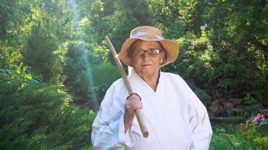 Parkta katanalı bir kimono giymiş yaşlı bir kadın. Bahçede katana ile antrenman yapan yaşlı bir kadının portresi. Yaşlılık, spor, doğa kavramı..  