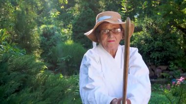 Parkta katanalı bir kimono giymiş yaşlı bir kadın. Bahçede katana ile antrenman yapan yaşlı bir kadının portresi. Yaşlılık, spor, doğa kavramı..  