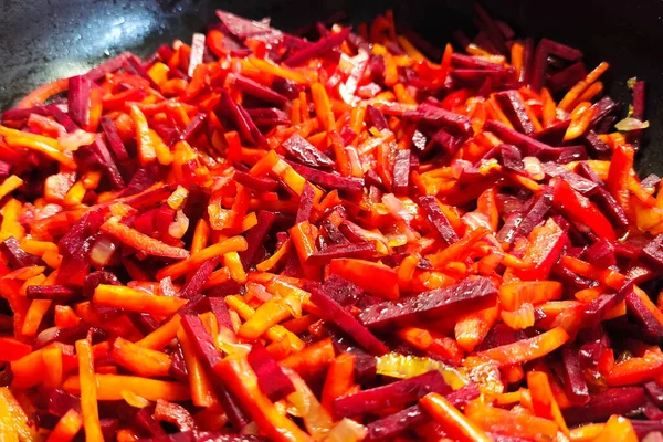 Cooking vegan healthy food from vegetables. Chopped carrots with beetroot in a frying pan.