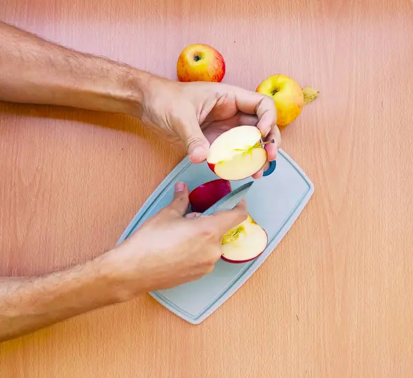 Close up male hands cut an apple into slices. Top view of preparing fruits over the kitchen table.