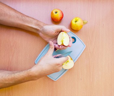Erkek eli kapat ve elmayı dilimlere ayır. Mutfak masasının üstünde meyve hazırlama manzarası.