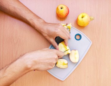 Erkek eli kapat ve elmayı dilimlere ayır. Mutfak masasının üstünde meyve hazırlama manzarası.