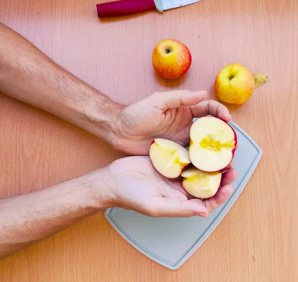 Close up male hands cut an apple into slices. Top view of preparing fruits over the kitchen table.