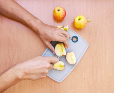 Erkek eli kapat ve elmayı dilimlere ayır. Mutfak masasının üstünde meyve hazırlama manzarası.