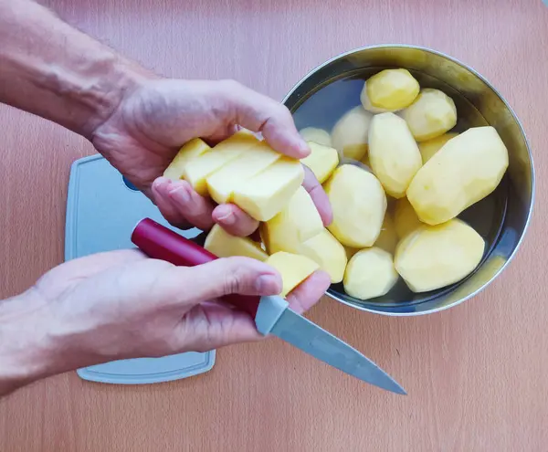 Man holding and peeling potato. Hands cutting potatoes at kitchen to prepare a recipe.