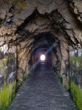 Huzurlu bir taş tünel ziyaretçileri karanlık geçidini keşfetmeye davet ediyor. En uçtaki parlak ışık, yamaçtaki doğal çevreyle çevrelenmiş..