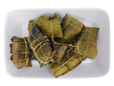 Delicious tamales, meticulously wrapped in banana leaves and tied with twine, rest in a white rectangular dish.  A vibrant overhead shot, perfect for food blogs, culinary websites, and recipe books. clipart