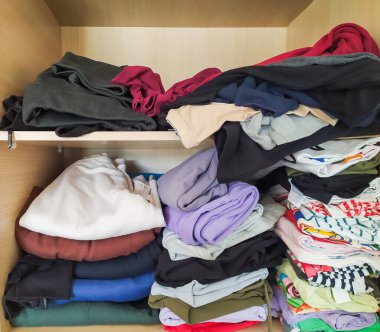 Düzgünce dizilmiş ve gelişigüzel katlanmış giysiler ahşap bir dolabı dolduruyor..