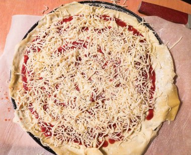 Üstünde domates sosu ve dilimlenmiş mozzarella peyniri olan ev yapımı pizza hamuru fırınlanmaya hazır. Yemek blogları, yemek tarifi web siteleri veya mutfak temalı projeler için mükemmel.