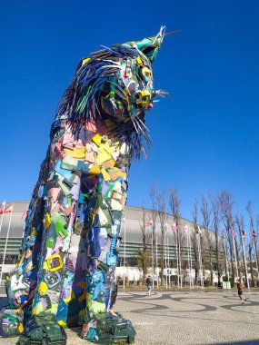 Canlı, büyük ölçekli geri dönüşümlü kedi heykeli açık mavi gökyüzüne karşı gururla duruyor. Göz alıcı sanat kurulumu, çevre, kentsel veya sanatsal projeler için mükemmel.