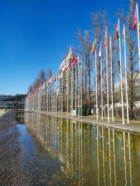 Uluslararası bayrakların ve modern mimarinin sakin bir su özelliğinde sakin bir yansıması. Küresel birlik, diplomasi, seyahat veya kentsel manzara kavramları için mükemmel.