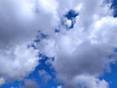 Pofuduk beyaz ve koyu gri kümülüs bulutlarının canlı mavi gökyüzüne karşı durduğu dramatik bulutlar. Arkaplan, web siteleri ya da herhangi bir proje için mükemmel