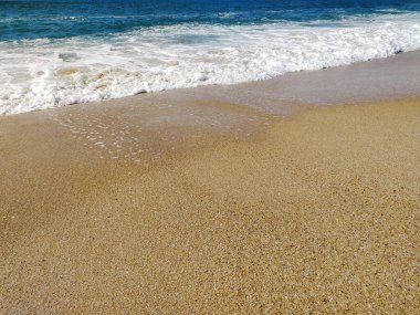 Kumlu sahil, yumuşak dalgaların parlak ve berrak bir gökyüzünün altında kıyıya ulaştığı sahil boyunca uzanır ve ziyaretçiler için huzurlu bir atmosfer yaratır..