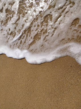 Güneş doğmaya başladığında, yumuşak dalgalar kumlu kıyıya vurur, parlak su ve kumlu dokularla güzel bir kontrast yaratır..