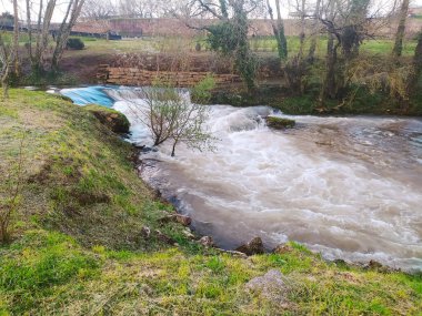 Serene nehri taştan bir barajın üzerine dökülüyor, yemyeşil ve çıplak kış ağaçlarının arasına yerleşmiş. Akan su, bir sükunet ve zamanın akışını anımsatıyor..