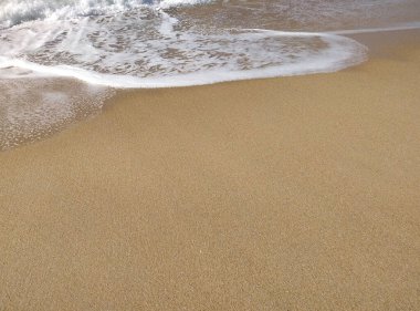 Güneş doğmaya başladığında, yumuşak dalgalar kumlu kıyıya vurur, parlak su ve kumlu dokularla güzel bir kontrast yaratır..