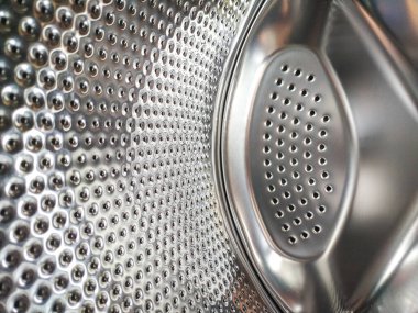 Metalik bir çamaşır makinesinin iç kısımlarına yakın çekim. Endüstriyel, temiz ve modern estetik. Hijyen, cihaz, doku veya desenle ilgili içerik için kullan.