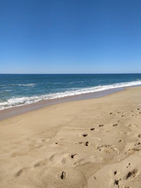 Kumlu sahil, yumuşak dalgaların parlak ve berrak bir gökyüzünün altında kıyıya ulaştığı sahil boyunca uzanır ve ziyaretçiler için huzurlu bir atmosfer yaratır..