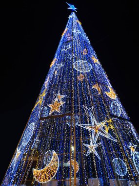 Çarpıcı mavi LED Noel ağacı gece bir şehir meydanını aydınlatıyor. Bayram tebrik kartları, web siteleri veya sosyal medya için harika bir ortam..