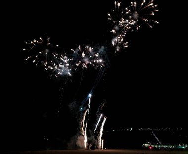 Karanlık bir plajın üzerindeki gece gökyüzünü aydınlatan muhteşem havai fişekler. Parlak ışık patlamaları, canlı bir kutlama sahnesi yaratır. Tatil, olay ve kutlama temaları için mükemmel..