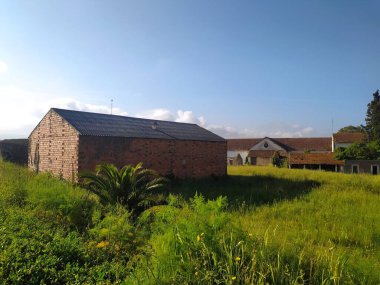 Bu sakin kırsal alandan kırsal bir cazibe yayılıyor. Eski tuğla binalar, berrak bir gökyüzünün altında sıcak güneş ışığıyla yıkanmış canlı yeşil bir çayırın ortasında duruyor. Huzur hissi uyandırıyor..